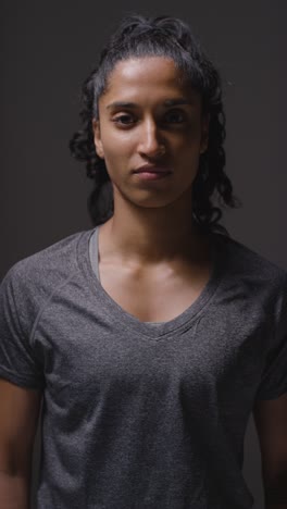 Vertical-Video-Studio-Shot-Of-Woman-Wearing-Sports-Clothing-Against-Dark-Background-Warming-Up